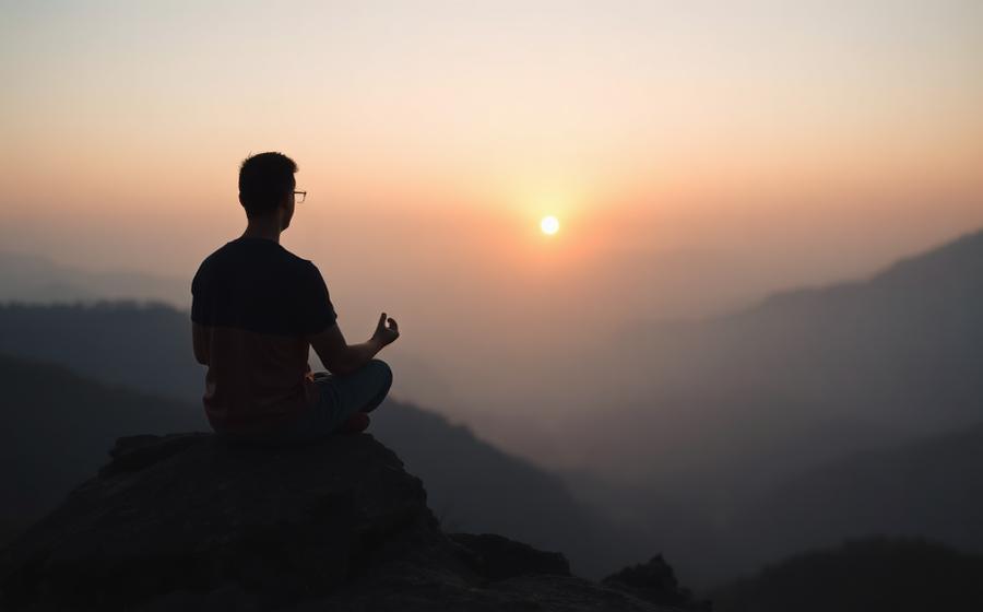 Persona in meditazione su una roccia davanti alle montagne